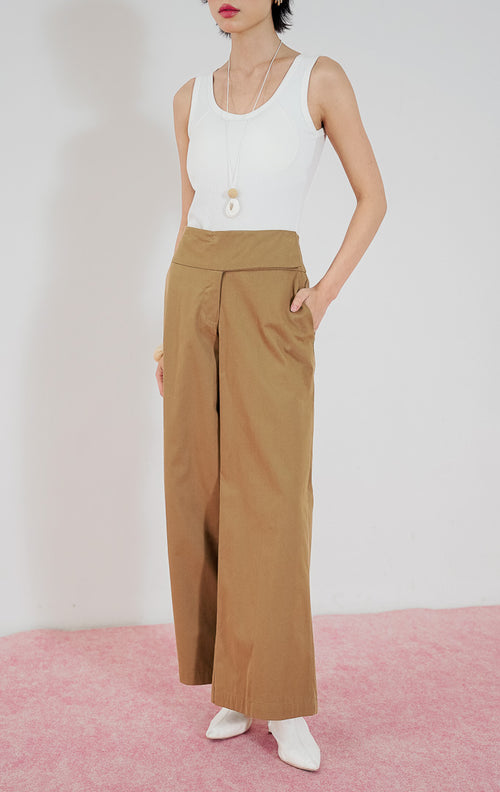 Celana panjang wanita Taffyra Pants warna cokelat (brown) dari This Is April dengan potongan high-waisted dan kaki lebar (wide leg), dipadukan dengan tank top putih.