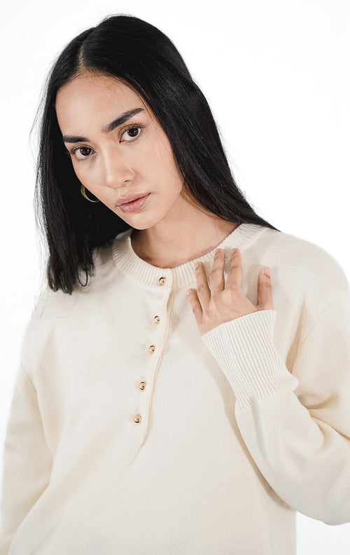 Model mengenakan Talia Cardigan warna ivory, atasan rajut lengan panjang dengan detail kancing emas kecil di bagian depan atas dan siluet rapi.