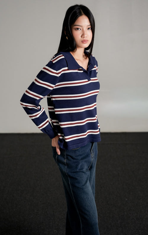 Tayden Sweater Navy, atasan rajut biru navy motif garis merah dan putih dengan kerah polo, dipadukan dengan celana jeans wide-leg gelap.
