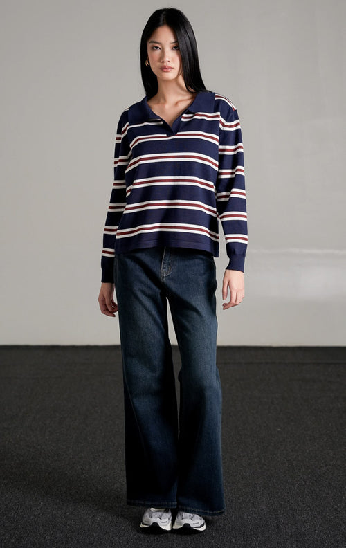 Tayden Sweater Navy, atasan rajut biru navy motif garis merah dan putih dengan kerah polo, dipadukan dengan celana jeans wide-leg gelap.