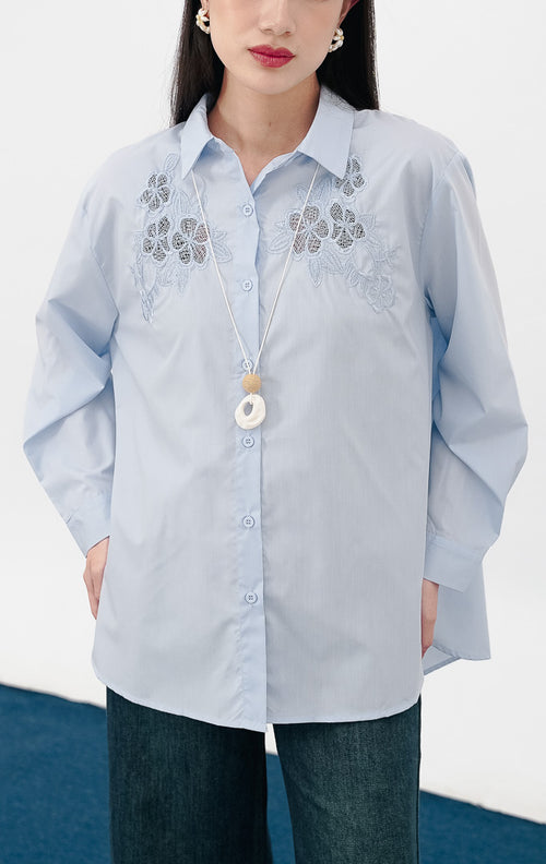 Close-up model mengenakan Tessa Top warna baby blue, kemeja katun lengan panjang dengan detail bordir bunga lace transparan yang cantik di sisi kanan dan kiri dada.