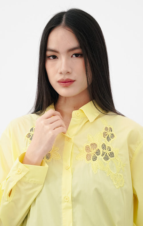 Close-up model mengenakan Tessa Top warna yellow, kemeja katun lengan panjang dengan detail bordir bunga lace transparan warna kuning senada di bagian dada.