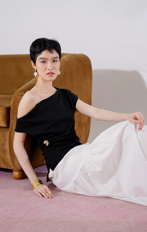Tampak depan This Is April Airana Top warna hitam, atasan wanita berbahan rajut dengan desain kerah drape berlipat dan detail aksen bros emas di bagian samping pinggang. 