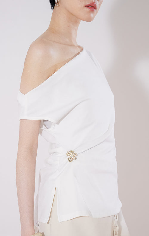 Tampak depan This Is April Airana Top warna putih, atasan wanita berbahan rajut dengan desain kerah drape berlipat dan detail aksen bros emas di bagian samping pinggang. 