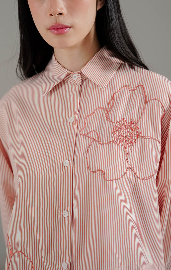 Amour Top Pink Peach dari This Is April, kemeja lengan panjang motif garis warna peach dengan detail bordir bunga besar dan potongan asimetris.