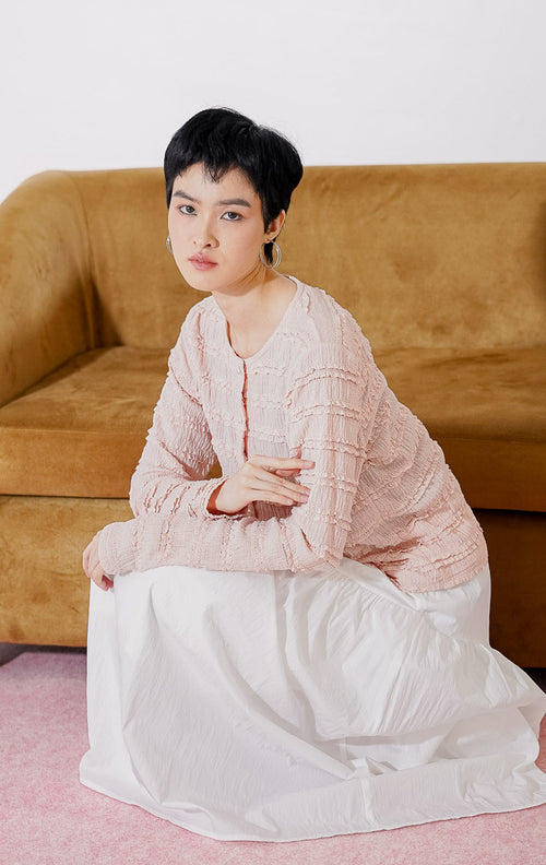 Outer crop wanita lengan panjang Anandra Top dari This Is April berwarna dusty pink dengan detail tekstur ruffle renda horizontal berlapis, kancing depan mutiara, dan material sheer menerawang, digantung di rak pakaian 