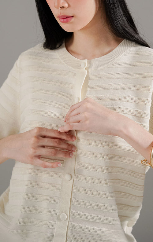 Annalina Cardigan Ivory dari This Is April, atasan rajut lengan pendek warna putih ivory dengan detail garis tekstur benang timbul dan kancing depan.