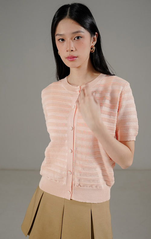 Annalina Cardigan Pink Peach dari This Is April, atasan rajut lengan pendek warna peach dengan motif garis benang timbul dan kancing depan.