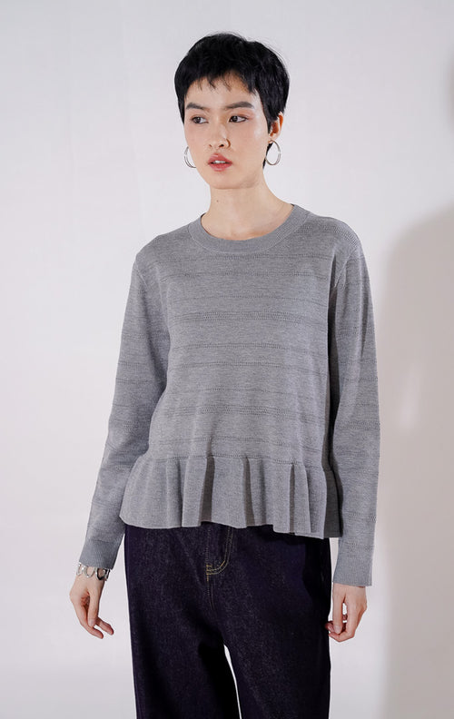 Sweater rajut wanita lengan panjang Arkiana Sweater dari This Is April berwarna abu-abu dengan motif garis berlubang (perforated) horizontal dan detail potongan kerut (ruffle/peplum) di bagian bawah 