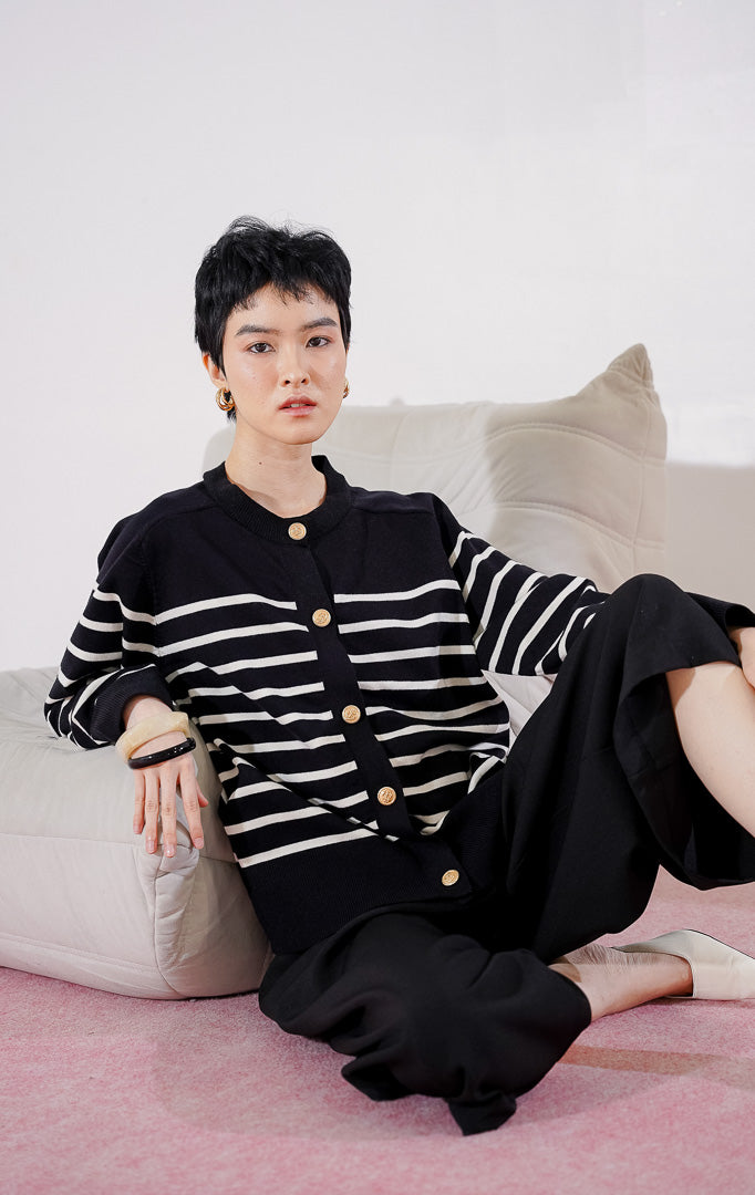 Tampak depan This Is April Aurelie Cardigan warna hitam, cardigan lengan panjang dengan motif garis putih horizontal, kerah bulat, dan detail kancing depan berwarna emas.