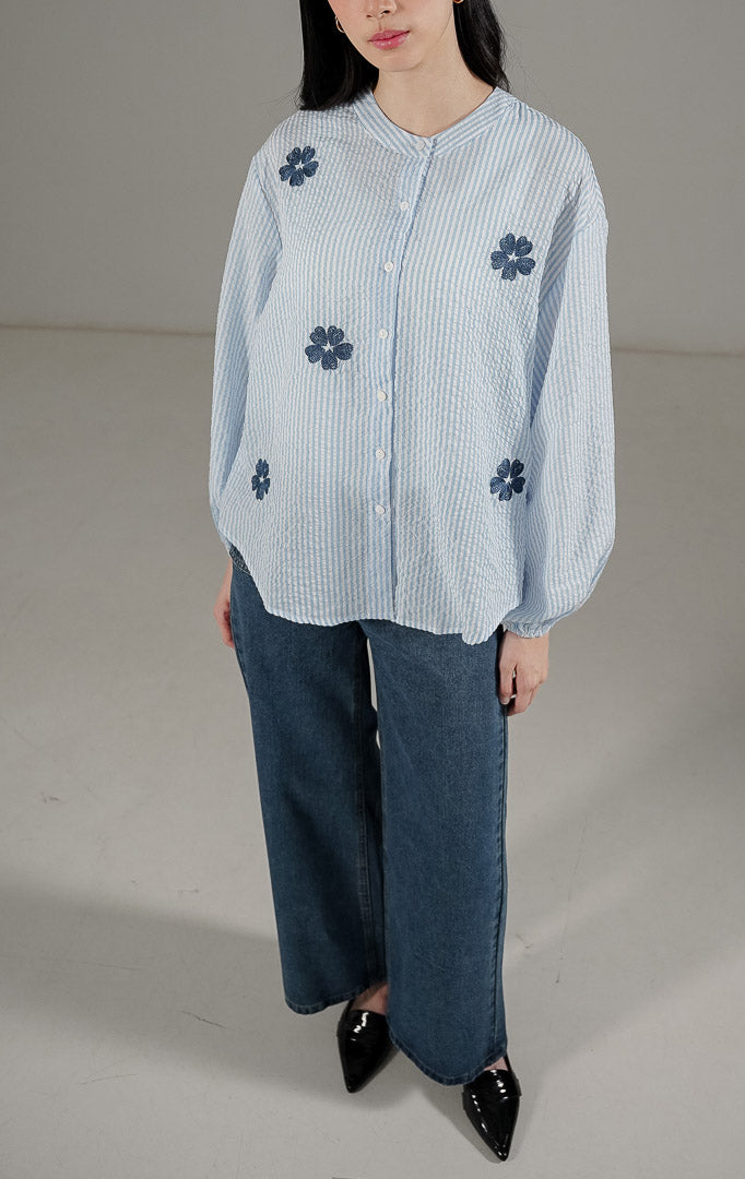 Azriel Top Blue dari This Is April, kemeja stripe biru putih lengan panjang dengan detail bordir bunga hitam dan pergelangan tangan karet.