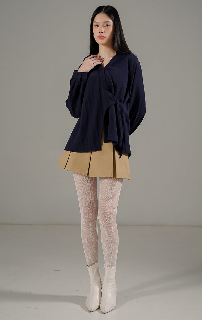 Bryanna Top Navy, atasan blus lengan panjang wanita warna biru dongker dengan kerah V dan detail tali pengikat di bagian tengah dan samping untuk merampingkan pinggang.