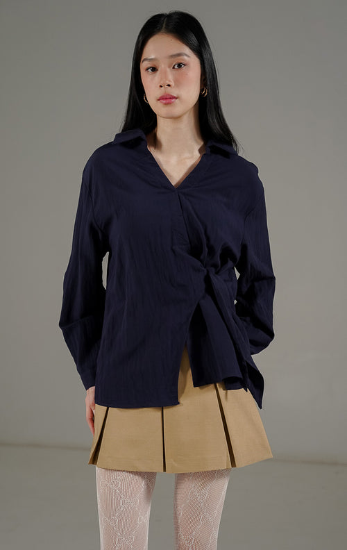 Bryanna Top Navy, atasan blus lengan panjang wanita warna biru dongker dengan kerah V dan detail tali pengikat di bagian tengah dan samping untuk merampingkan pinggang.