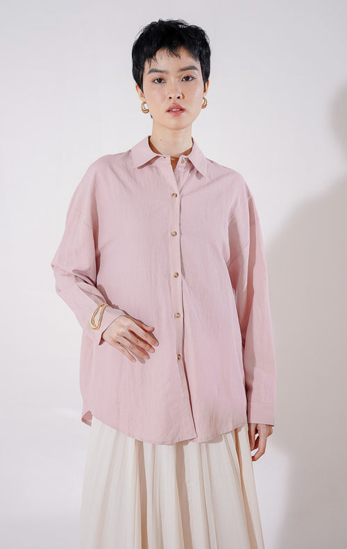 Kemeja wanita lengan panjang Caelia Top dari This Is April berwarna dusty pink dengan detail kancing depan, digantung di rak pakaian. 