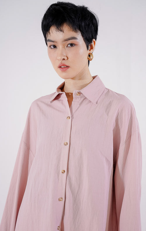 Kemeja wanita lengan panjang Caelia Top dari This Is April berwarna dusty pink dengan detail kancing depan, digantung di rak pakaian. 