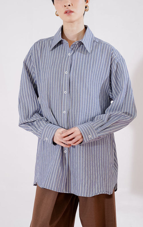 Kemeja wanita lengan panjang Carmela Top dari This Is April berwarna navy dengan motif garis vertikal putih tipis (pin stripes), bertekstur crinkle halus, dilengkapi kerah klasik dan kancing depan, digantung di rak pakaian. 