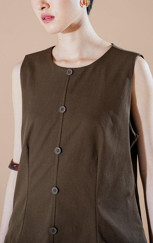 Cayden Dress Dark Brown dari This Is April, gaun tanpa lengan warna cokelat tua dengan detail rok lipit (pleated) bertumpuk dan kancing depan.