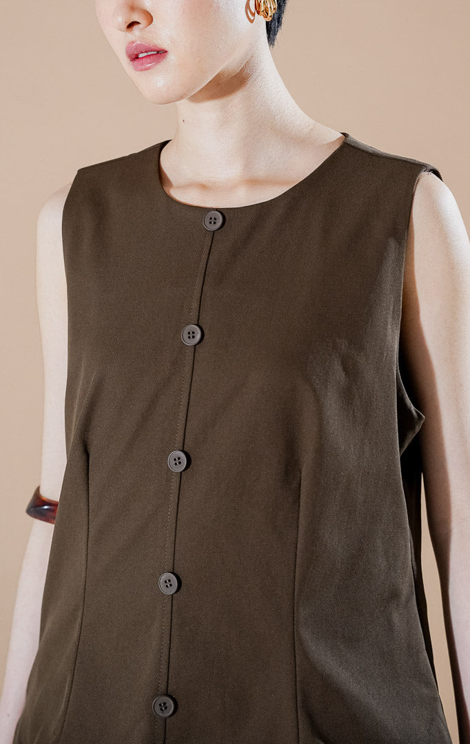 Cayden Dress Dark Brown dari This Is April, gaun tanpa lengan warna cokelat tua dengan detail rok lipit (pleated) bertumpuk dan kancing depan.