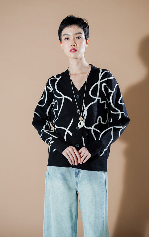 Coralina Cardigan Black dari This Is April, cardigan rajut V-neck warna hitam dengan motif garis abstrak putih dan kancing depan.