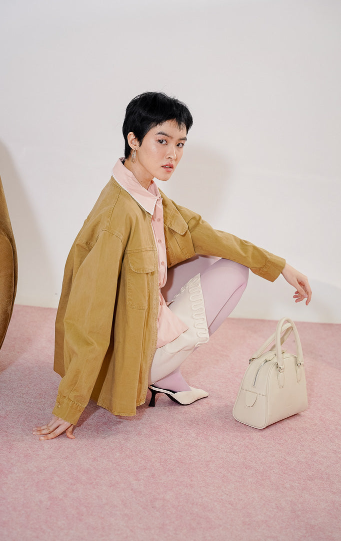 Kemeja wanita lengan panjang Dahlia Top dari This Is April berwarna khaki berbahan katun twill dengan dua kantong dada fungsional dan kancing depan, digantung di rak pakaian. 