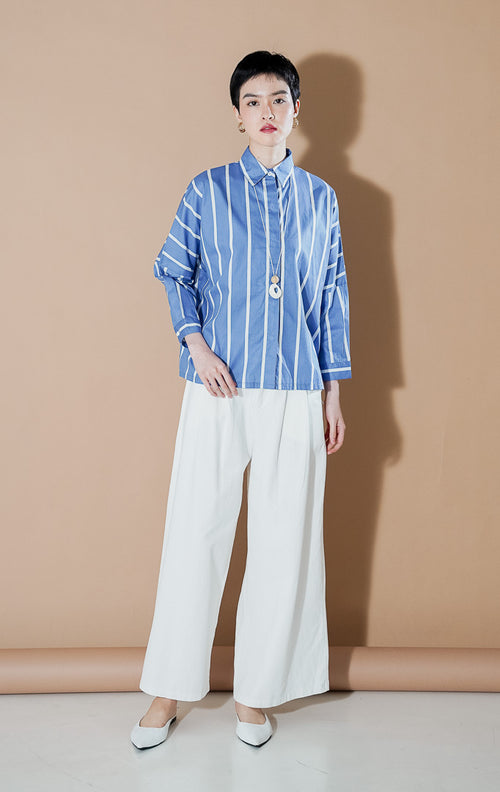 Deliora Top Blue dari This Is April, kemeja katun lengan panjang siluet boxy warna biru dengan motif garis vertikal putih dan kancing depan.