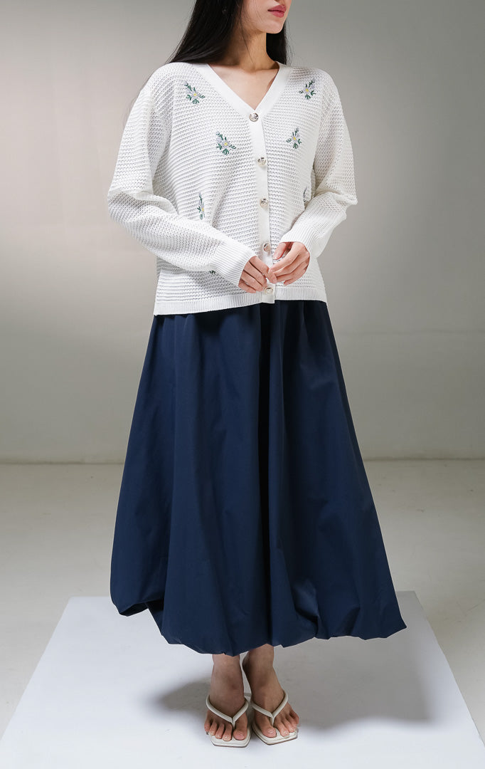 Kardigan rajut lengan panjang wanita This Is April Dorian Cardigan warna putih, model jaring transparan dengan kerah v-neck, kancing depan warna emas, dan detail bordir motif bunga kecil warna ungu. 