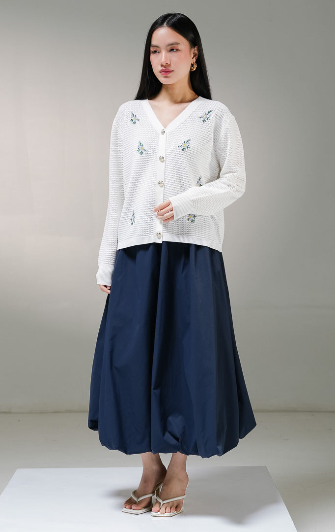 Kardigan rajut lengan panjang wanita This Is April Dorian Cardigan warna putih, model jaring transparan dengan kerah v-neck, kancing depan warna emas, dan detail bordir motif bunga kecil warna ungu. 