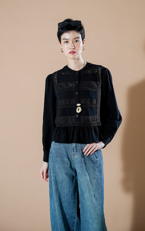 Eliot Top Black dari This Is April, blus katun lengan panjang warna hitam dengan detail panel bordir di dada dan aksen ruffle di bagian bawah (hem).