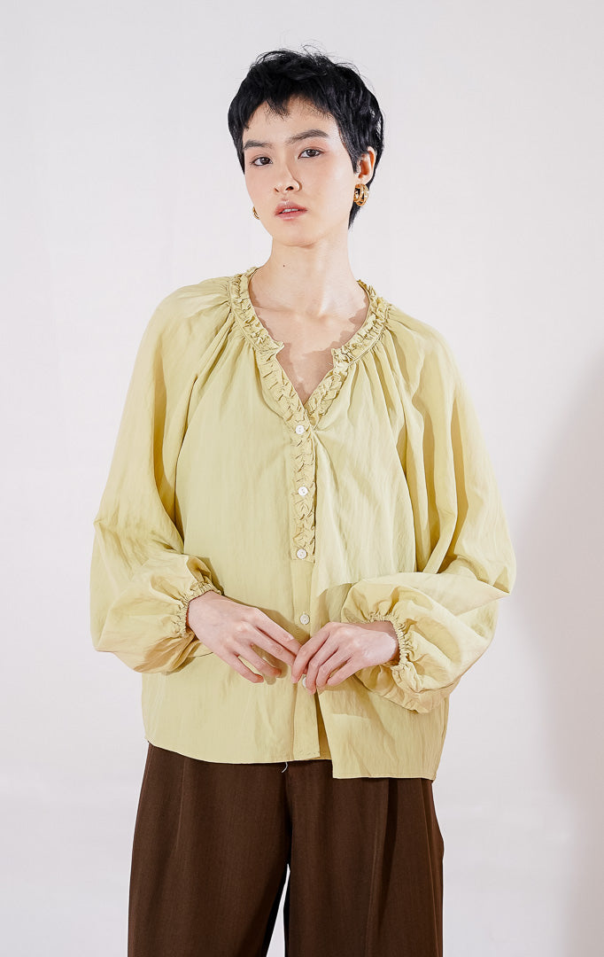 Blouse lengan panjang wanita This Is April Eloise Top warna khaki berbahan katun, dengan kerah V-neck beraksen ruffle, kancing depan, dan ujung lengan karet. 