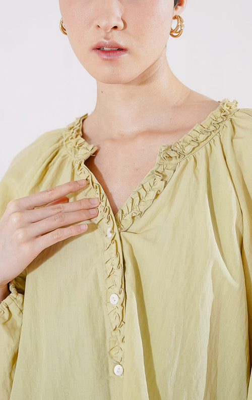 Blouse lengan panjang wanita This Is April Eloise Top warna khaki berbahan katun, dengan kerah V-neck beraksen ruffle, kancing depan, dan ujung lengan karet. 
