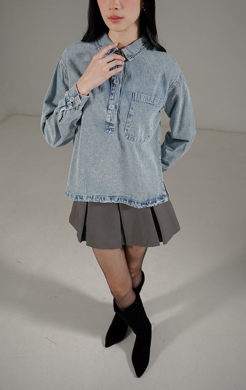 Atasan kemeja Elyse Top Denim wanita warna biru muda dari This Is April, dilengkapi kerah, kancing depan aktif parsial, dan saku dada fungsional.