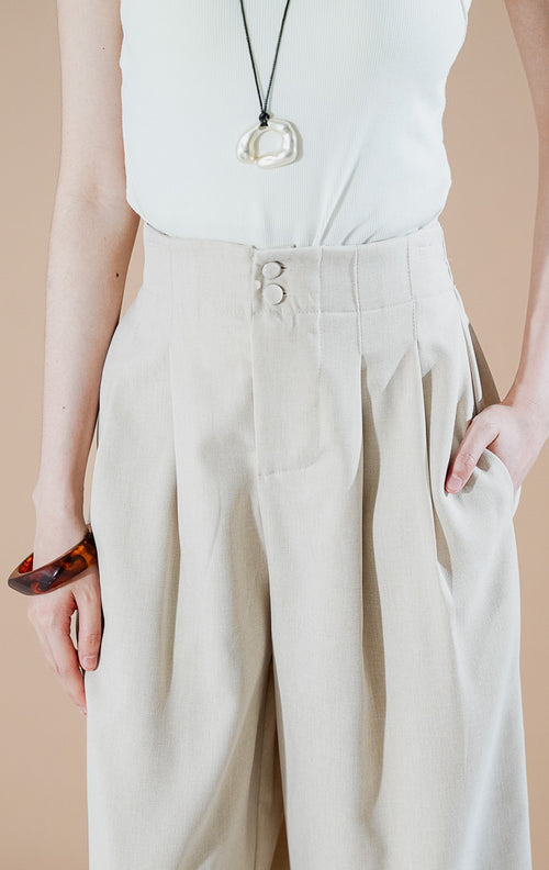 Endellion Pants Beige dari This Is April, celana panjang tailored wanita warna krem dengan detail dua kancing di pinggang, lipit depan (pleated), dan bahan katun terstruktur.