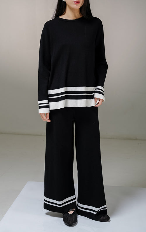 Setelan one set wanita This Is April Espera Set warna hitam, terdiri dari atasan sweater rajut lengan panjang kerah bulat dan celana panjang rajut dengan detail aksen garis horisontal warna putih di bagian ujung bawah.