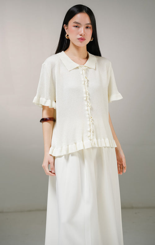 Atasan baju rajut lengan pendek wanita This Is April Eudora Top warna ivory (krem), model ribbed knit polo shirt berkerah dengan detail aksen kerut ruffle bergelombang di sepanjang kancing depan, ujung lengan, dan ujung bawah baju. 