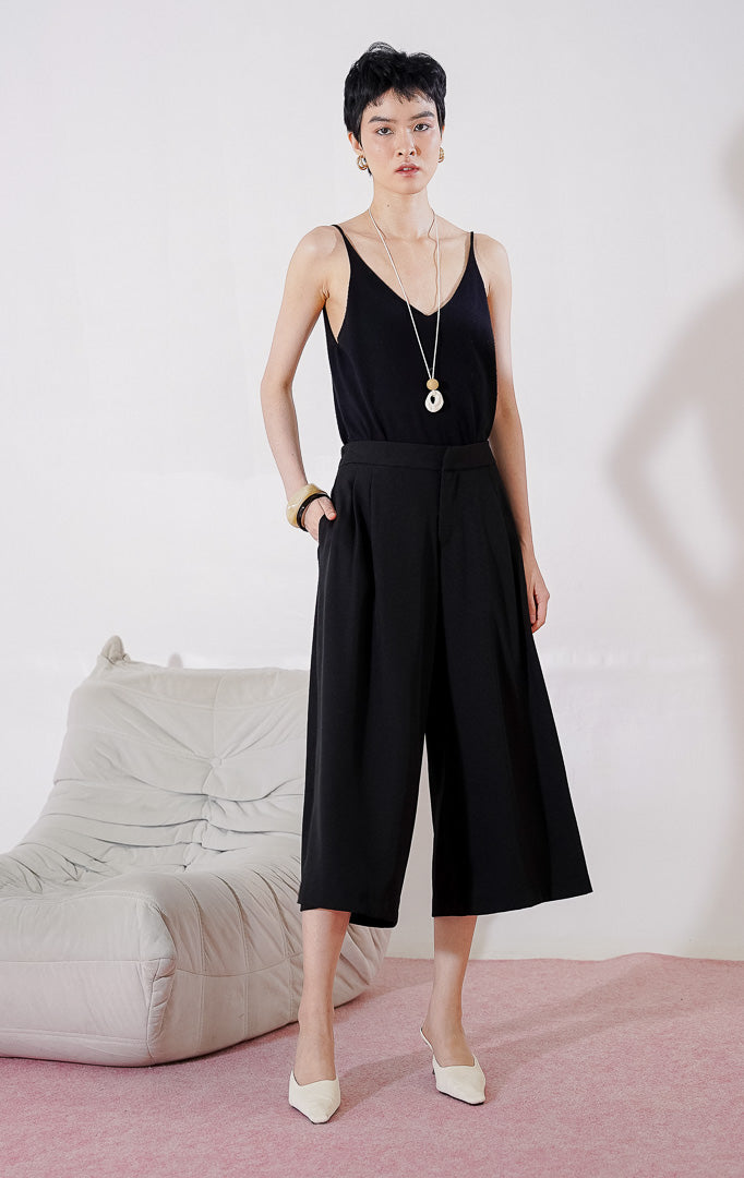 Celana bermuda wanita This Is April Hiraeth Pants warna hitam, berpotongan wide-leg yang longgar, dengan detail lipit rapi di bagian depan dan pinggang karet di bagian belakang. 