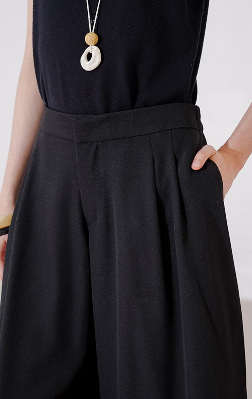 Celana bermuda wanita This Is April Hiraeth Pants warna hitam, berpotongan wide-leg yang longgar, dengan detail lipit rapi di bagian depan dan pinggang karet di bagian belakang. 