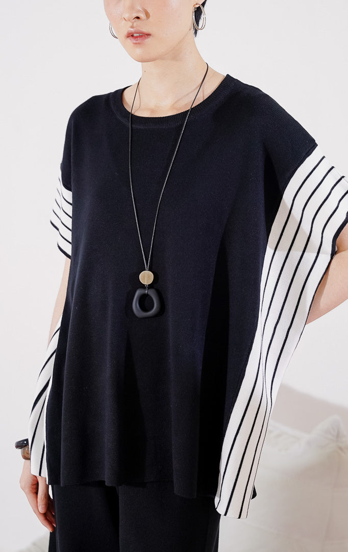 Baju setelan rajut wanita Kanza Set Black dari This Is April berwarna hitam dengan detail garis vertikal putih di bagian lengan, digantung di rak pakaian. 