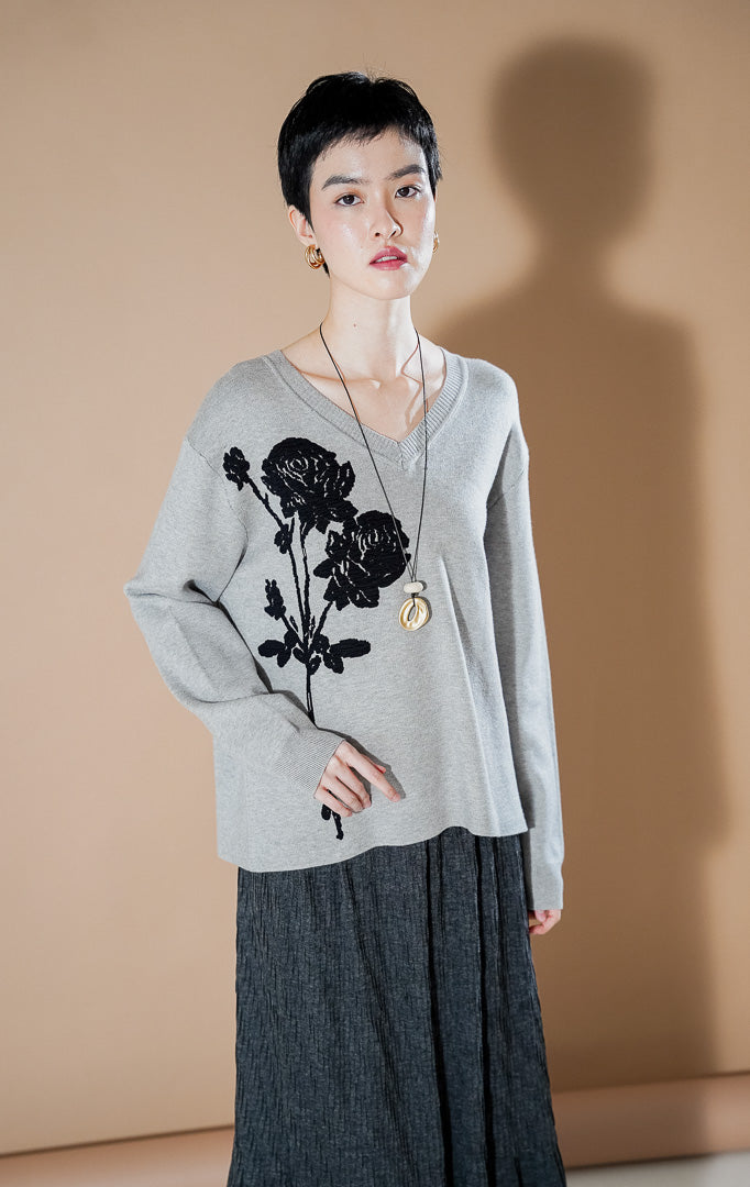 Lulie Sweater Grey dari This Is April, sweater rajut leher V-neck warna abu-abu dengan detail bordir bunga mawar hitam yang besar di bagian depan.