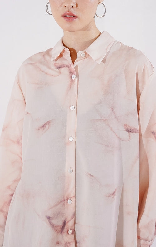 Kemeja wanita lengan panjang Manon Top dari This Is April dengan motif gradasi warna peach dan putih yang lembut, berbahan sheer menerawang dengan kancing depan, digantung di rak pakaian. 