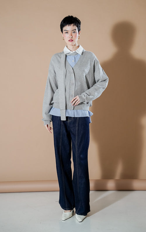 Model wanita mengenakan This Is April Marianne Cardigan Grey, kardigan rajut V-neck abu-abu dengan kancing depan, detail syal leher menyatu, dan motif rajutan chevron.