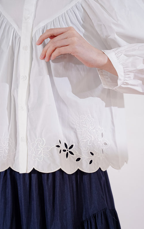 Blouse crop lengan panjang wanita This Is April Marvie Top warna putih berbahan katun, dengan kerah shanghai, kancing depan, jahitan yoke di dada, dan detail bordir bunga pada ujung bawah 