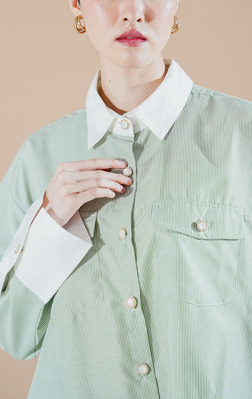 Merveille Top Green Stripe dari This Is April, kemeja lengan panjang motif salur hijau sage dengan kerah dan manset putih kontras serta detail kancing mutiara bingkai emas.