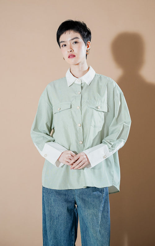 Merveille Top Green Stripe dari This Is April, kemeja lengan panjang motif salur hijau sage dengan kerah dan manset putih kontras serta detail kancing mutiara bingkai emas.