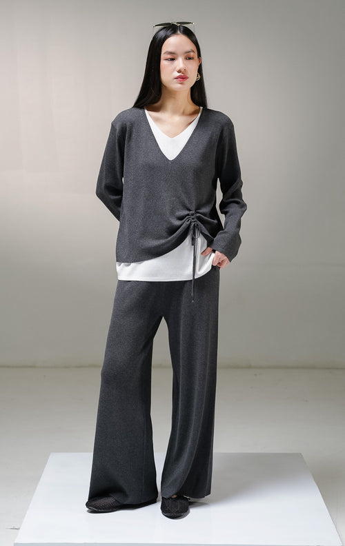 Setelan one set wanita This Is April Millicent Set warna abu-abu tua (dark grey), terdiri dari atasan sweater rajut lengan panjang kerah v-neck dengan aksen layer putih di leher dan ujung baju, serta celana panjang rajut senada. 
