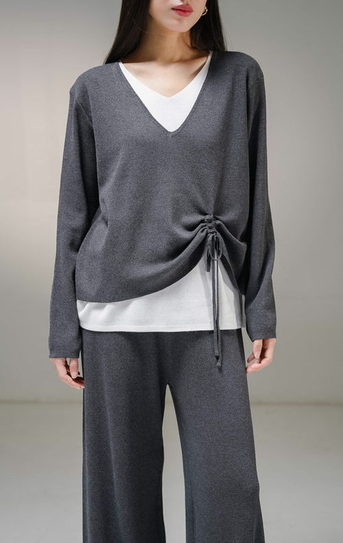 Setelan one set wanita This Is April Millicent Set warna abu-abu tua (dark grey), terdiri dari atasan sweater rajut lengan panjang kerah v-neck dengan aksen layer putih di leher dan ujung baju, serta celana panjang rajut senada. 