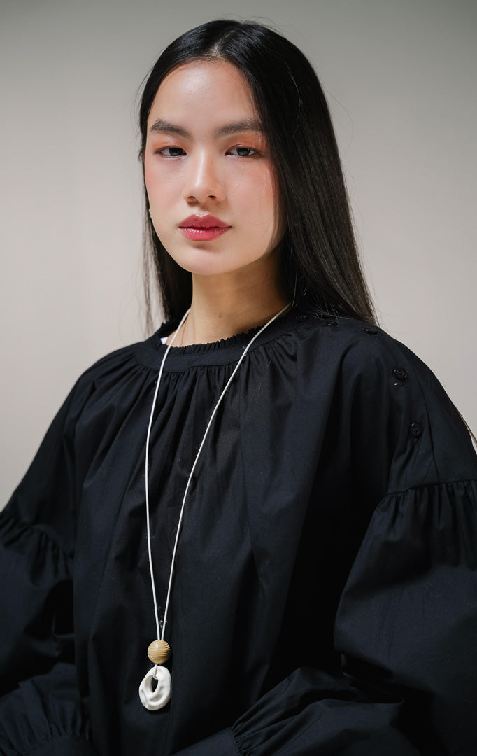 Blouse lengan panjang wanita This Is April Morgana Top warna hitam, model crewneck dengan detail kerutan penuh di sekeliling leher dan deretan kancing aktif di sisi bahu kiri. 