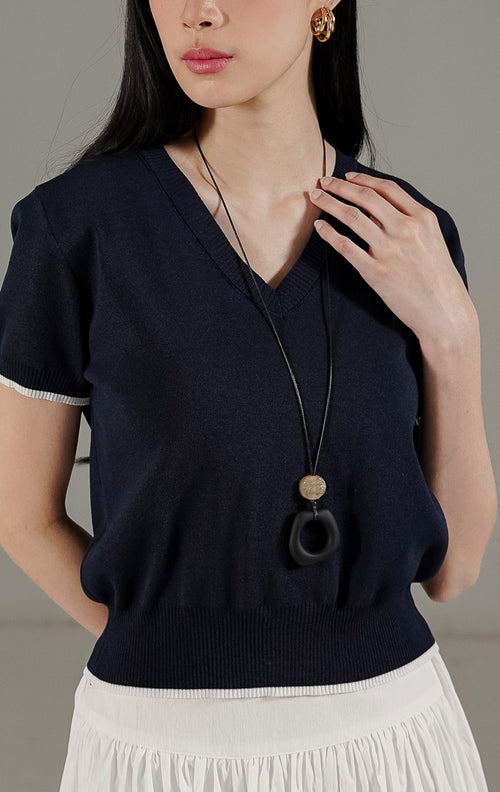 Morgane Top Navy dari This Is April, atasan rajut V-neck lengan pendek warna biru navy dengan detail garis putih kontras pada ujung lengan dan pinggang.