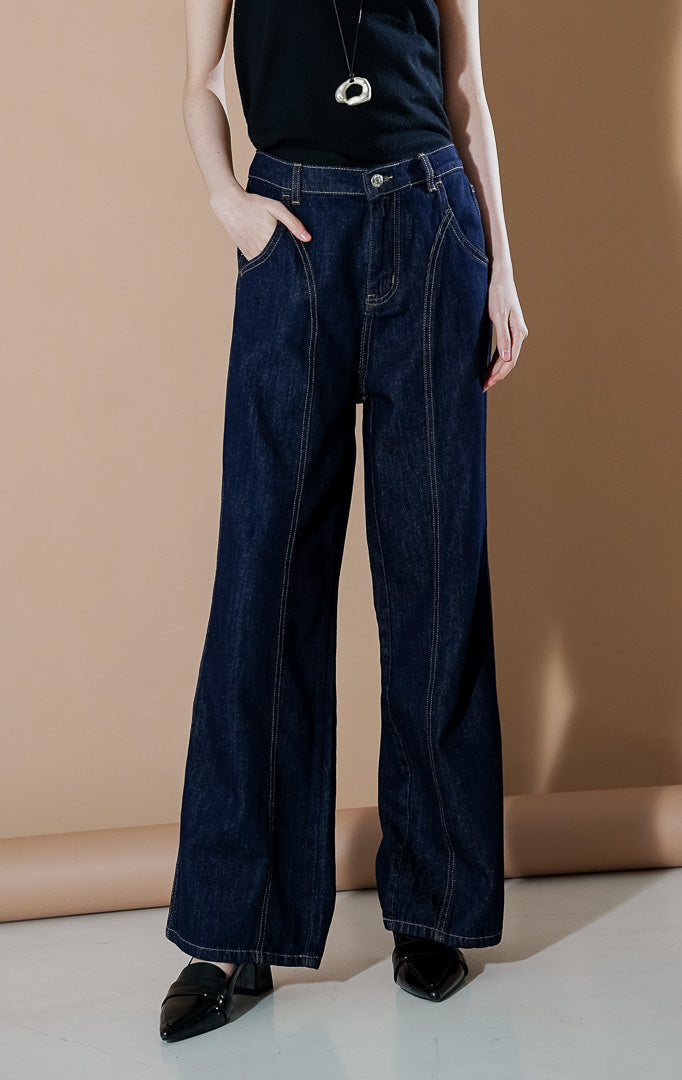 Nadette Pants Indigo dari This Is April, celana jeans wanita warna biru indigo tua dengan detail jahitan cokelat kontras di bagian depan dan siluet kaki lebar.