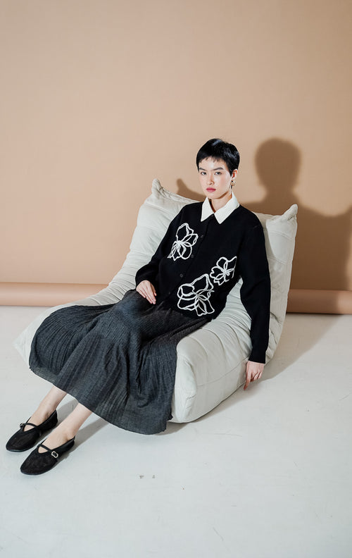 Peppie Cardigan Black dari This Is April, cardigan rajut warna hitam dengan detail bordir bunga putih di bagian depan dan kancing aktif.