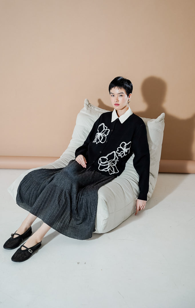 Peppie Cardigan Black dari This Is April, cardigan rajut warna hitam dengan detail bordir bunga putih di bagian depan dan kancing aktif.